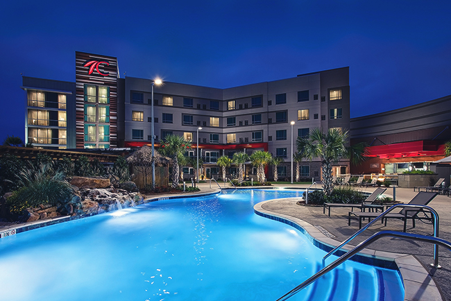 Choctaw Casino & Resort–Grant at night, glowing outdoor pool with palm trees and the hotel building in the background