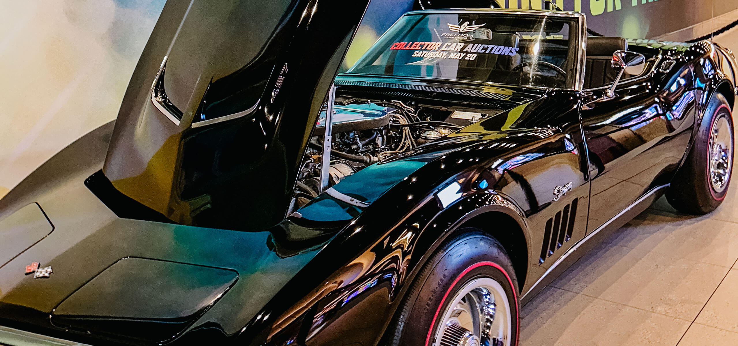 Classic black convertible sports car with hood open at an indoor ‘Collector Car Auctions’ display.