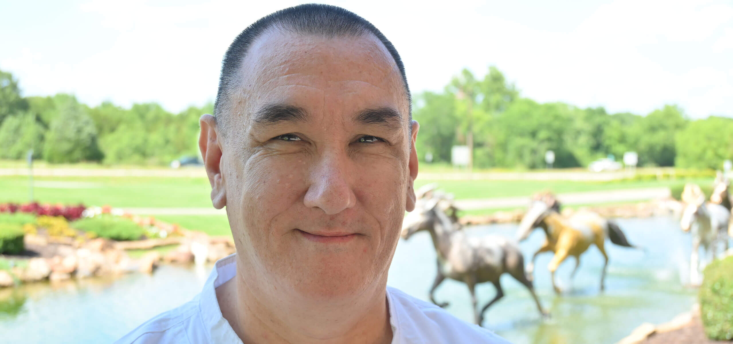 Portrait of Chef Byron Wilson outdoors, smiling in front of a pond with running horse statues.