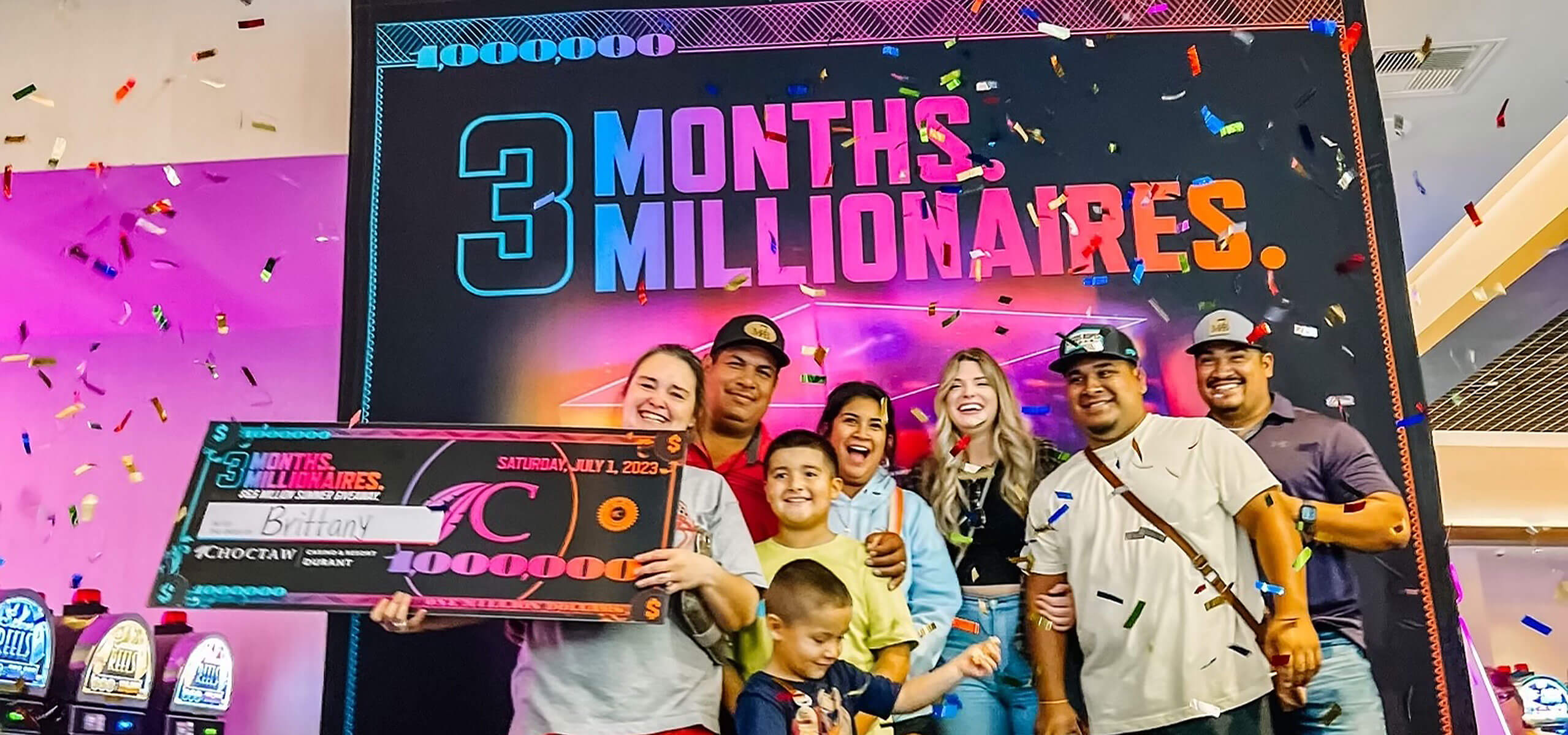 Group celebrating under ‘3 Months. Millionaires.’ sign; winner holds a giant $1,000,000 check as confetti falls.