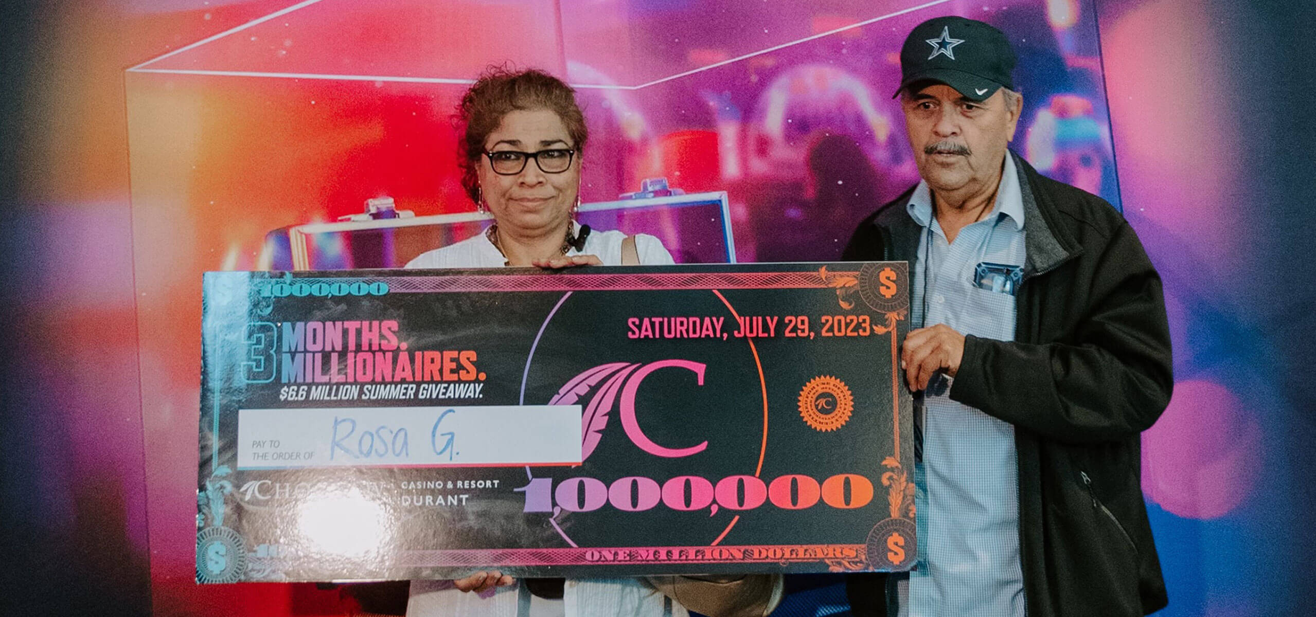Rosa Guia and partner hold a giant $1,000,000 check in front of a colorful backdrop.