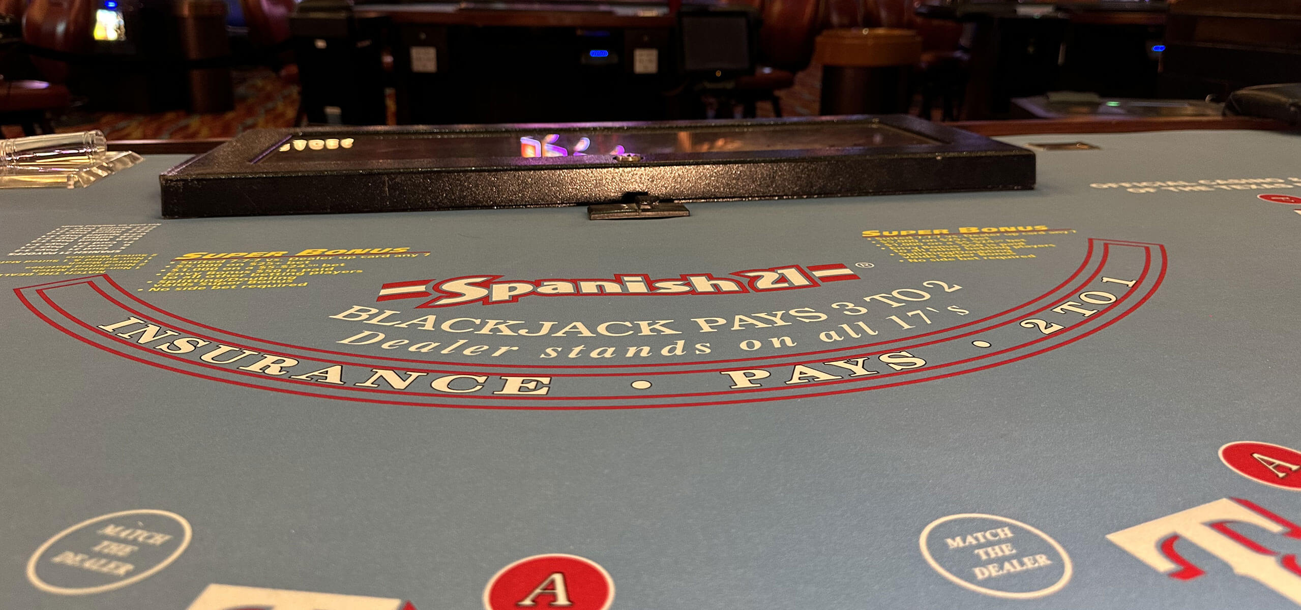 Spanish 21 blackjack table felt showing rules and payouts, with card slots and chip rack in the background