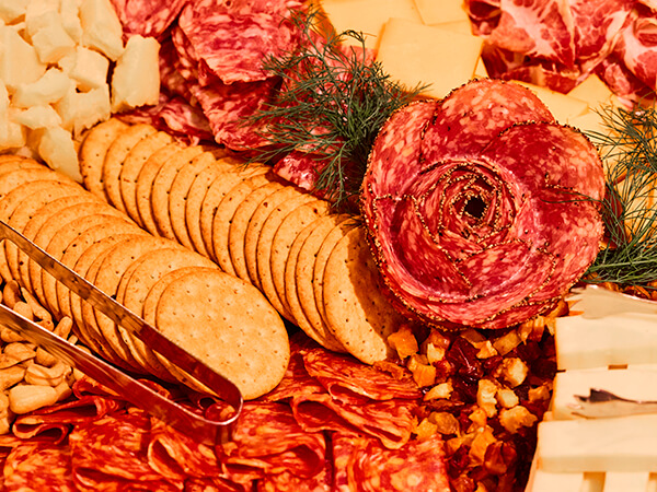 Charcuterie spread with a salami rose, sliced crackers, assorted cheeses, nuts, and fresh herbs