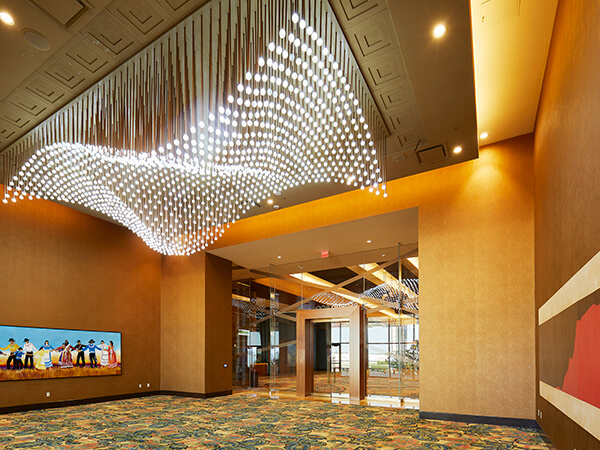 Lobby with a wave-like chandelier of hanging lights, warm-toned walls, patterned carpet, and glass double doors