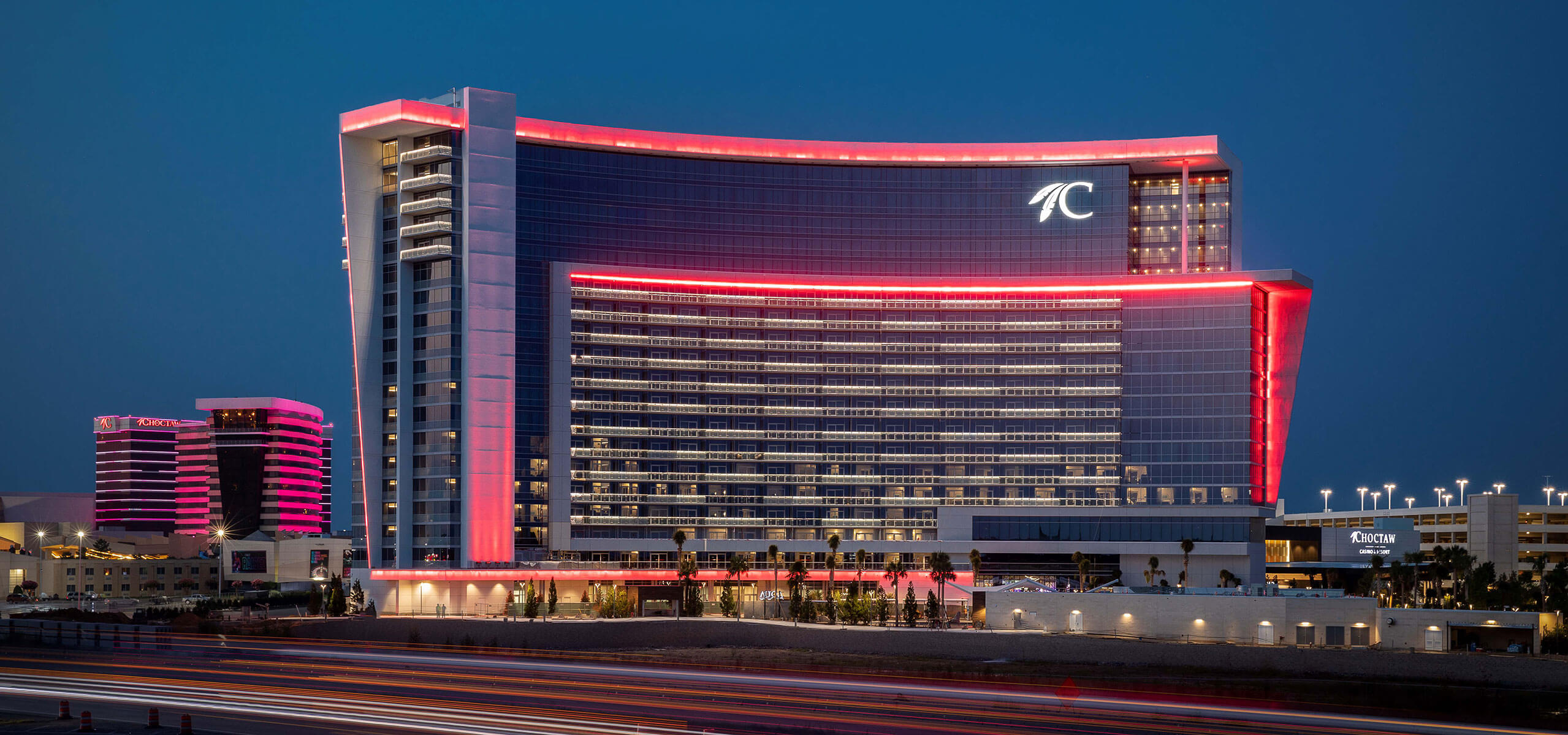 Choctaw Casino & Resort – Durant exterior at dusk with pink neon outlines tracing the tower and traffic light trails in front