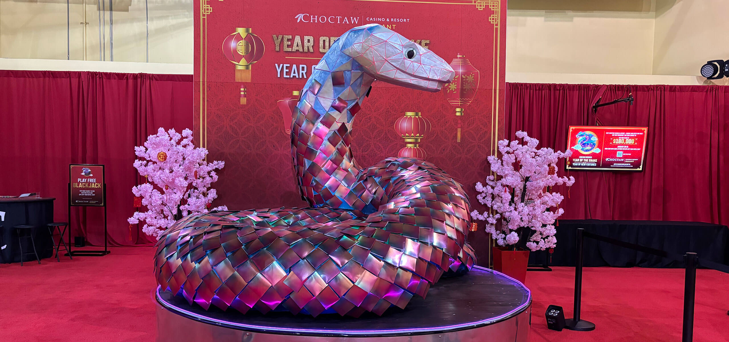 Iridescent ‘Year of the Snake’ sculpture coiled on a stage with pink cherry blossom trees and a red festival backdrop