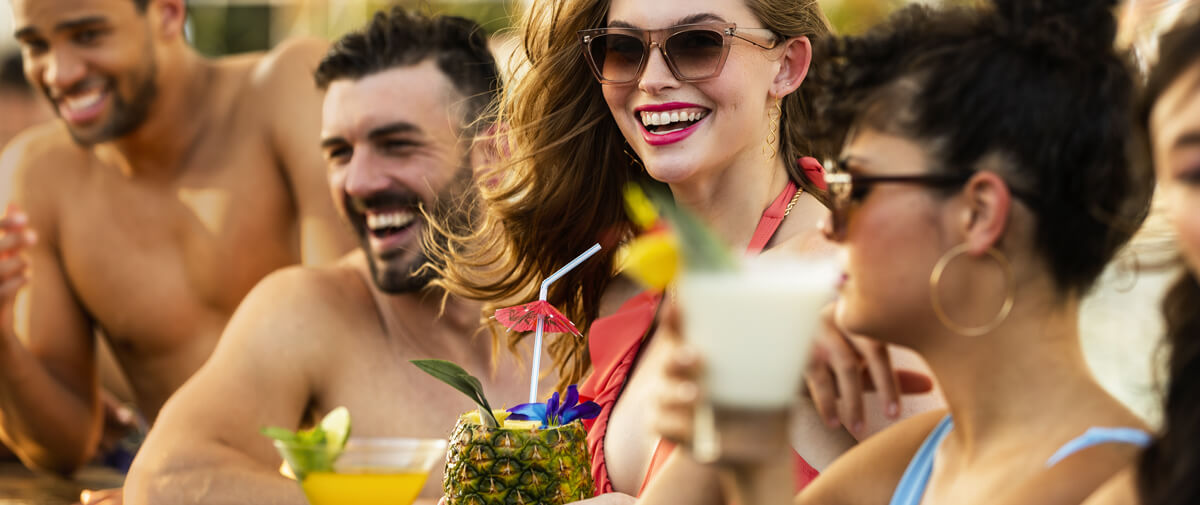 Friends laughing at a pool bar with tropical cocktails, including a pineapple drink with a paper umbrella